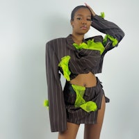 a black woman in a striped suit posing in front of a white wall