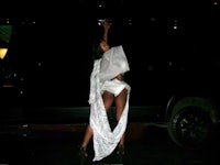 a woman in a white dress posing in front of a black car