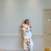 a woman in a white dress leaning against a wall